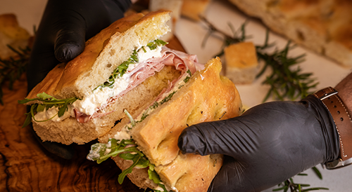 A focaccia with sandwich with mortadella, straciatella and rucola served on a wooden plate in San Rocco Bale cut in half